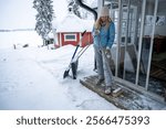 Woman wearing winter clothes using a broom to clear snow from a wooden porch. concept of outdoor chores
