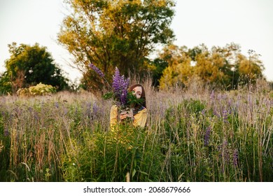 Woman wearing yellow coat with lupines flowers stay in high summer grass in rural meadow. Freedom new normal concept.