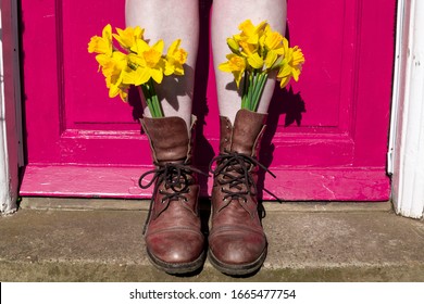 Woman Wearing Yellow Flowers In Brown Boots Against Pink Front Door. Feminine Quirky Fun Eye Catching British England Spring Summer Instagram Style Concept Idea