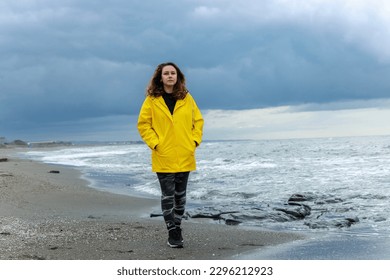Woman wearing yellow raincoat walking on the beach on a rainy day - Powered by Shutterstock