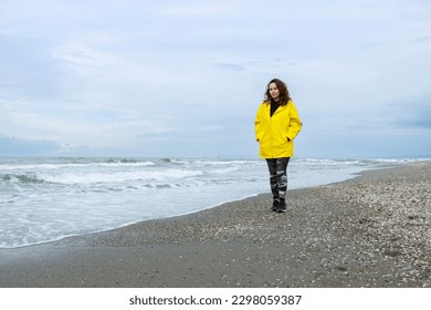 Woman wearing yellow raincoat walking on the beach on a rainy day - Powered by Shutterstock