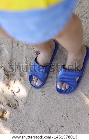 Woman wears blue slipper and stands on the beach