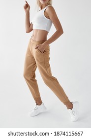 Woman Wears Khaki Pants. Fit Girl Is Standing In Beige Joggers