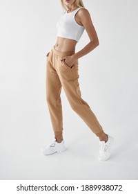 Woman Wears Khaki Pants. Fit Girl Is Standing In Beige Joggers