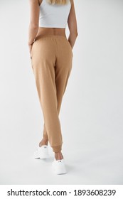 Woman Wears Khaki Pants. Fit Girl Is Standing In Beige Joggers