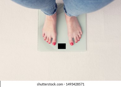 Woman is weighed on scales, female feet, top view, cropped image, toned