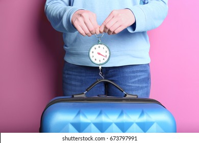 Woman Weighting Heavy Luggage On Color Background