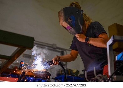 Woman welding iron with electric welding equipment in workshop, wearing protective gear - Powered by Shutterstock