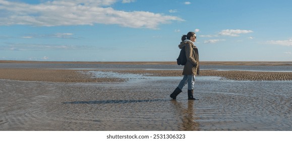 Woman in wellington boots walking on beach at low tide - Powered by Shutterstock