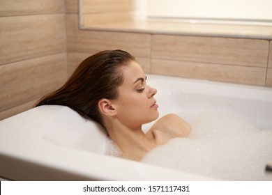 A Woman With Wet Hair Is Lying In A Bathtub With White Foam