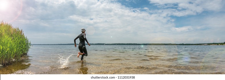 Woman In A Wetsuit Running Into The Water To Swim, Panorama