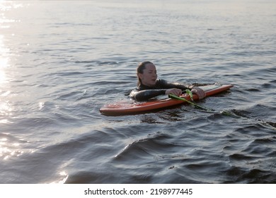 Woman In A Wetsuit Swim In The River With Board In Her Hands While Learning To Ride A Wakesurf