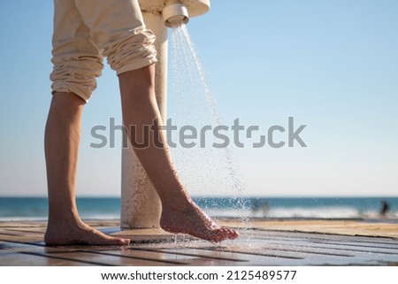 Woman wetting her feet with a shower to clean them from the sand