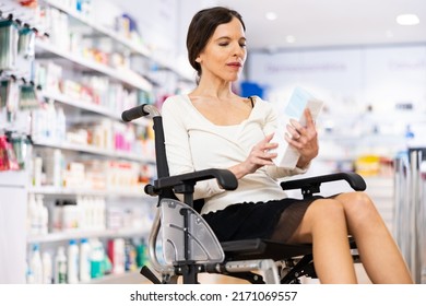 Woman In Wheelchair Holding Box With Medical Supplies, Reading Label Text About Ingredients And Directions At Drugstore