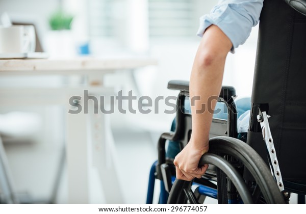 Woman in wheelchair next to an office desk, hand\
close up, unrecognizable\
person