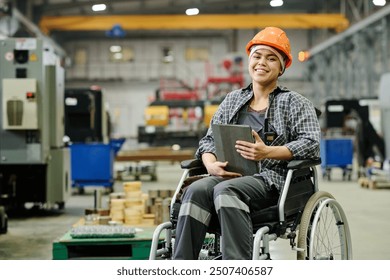 Woman in wheelchair wearing a hard hat and plaid shirt, smiling while holding clipboard in workshop, with industrial equipment and machinery in background - Powered by Shutterstock