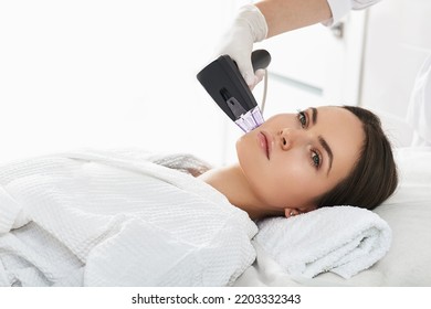 Woman while RF lifting procedure for her face skin tightening with cosmetologist at a beauty salon