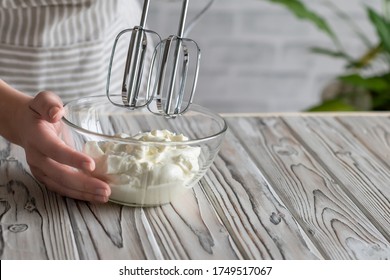 Woman Whipping Cream Using Electric Hand Mixer On The Gray Rustic Wooden Table  