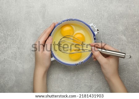 Woman whisking eggs at grey table, top view