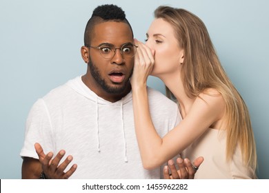 Woman whispering in African American man ear, telling unexpected news, shocked surprised boyfriend hearing unbelievable rumors from girlfriend, friends gossiping, isolated on studio background - Shutterstock ID 1455962282