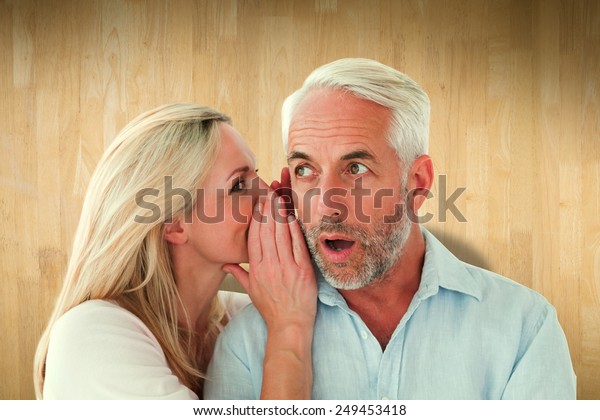 Woman whispering a secret to husband against wooden planks