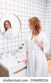 Woman In White Bathrobe Looking At Mirror In Bathroom