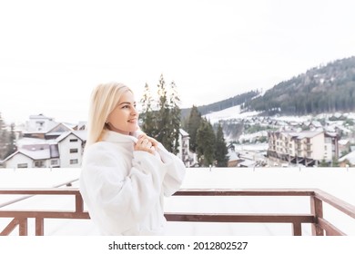 A Woman In A White Bathrobe Standing On The Balcony Of A SPA In Austria In Winter. She Has Wet Hair. She Is Enjoying The View On Mountains In Front Of Her. She Is Feeling Relaxed