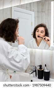 Woman In White Bathrobes Brushing Teeth In Front Of Mirror