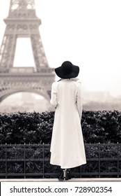 Woman In White Coat And Black Hat In Paris In Front Of The Eiffel Tower. Black And White Picture