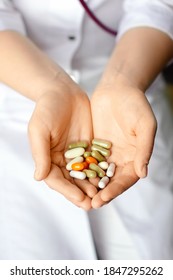 woman in white coat holding a handful of pills in palms close-up