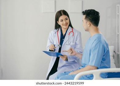 A woman in a white coat is talking to a man in a blue hospital gown. The woman is pointing to something on a clipboard - Powered by Shutterstock