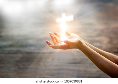 Woman with white cross in hands praying for blessing from god on sunlight background, hope concept