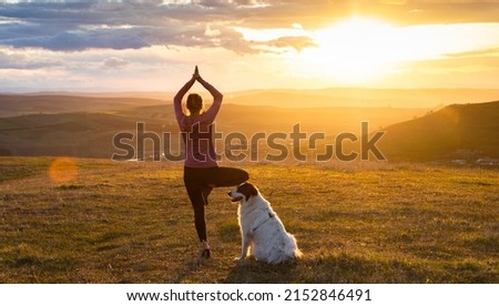 woman with white dog doing yoga at sunset tree pose  vrksasana