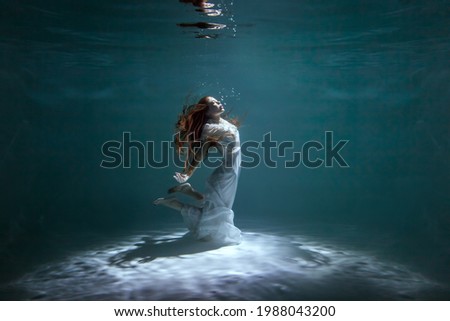 Woman in a white dress is dancing underwater while showing a show.