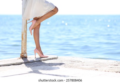 woman in white dress leaning standing by the sea side looking at the sea with stilettos