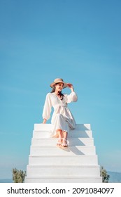 Woman In A White Dress Sitting On A White Staircase Extends Into Blue Sky