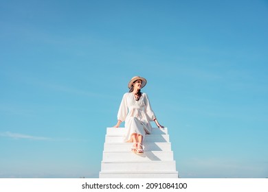 Woman In A White Dress Sitting On A White Staircase Extends Into Blue Sky