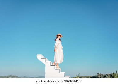 Woman In A White Dress Sitting On A White Staircase Extends Into Blue Sky