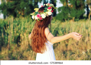 Woman in white dress standing in field wearing flower crown. Young forest inspired bride, bohemian girl