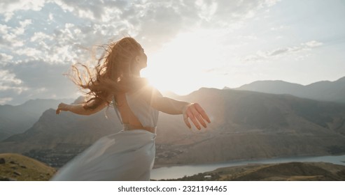 Woman in white dress standing on top of a mountain at sunset with raised hands while wind is blowing her dress and red hair - freedom, nature concept. Copy space - Powered by Shutterstock