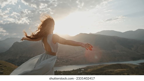 Woman in white dress standing on top of a mountain with raised hands while wind is blowing her dress and red hair - freedom, nature concept.Copy space - Powered by Shutterstock