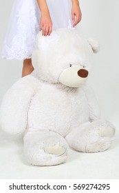 Woman in white dress stands with big toy bear in white studio, noface