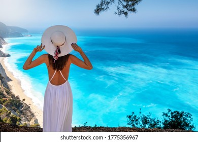 A Woman In White Dress And With Sunhat Gazes The Blue Fluorescent Sea Of The Famous Egremoi Beach And The Greek Island Of Lefkada, Ionian Islands