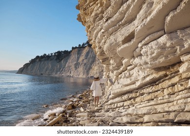 woman in white dress walking near shore on cliff edge