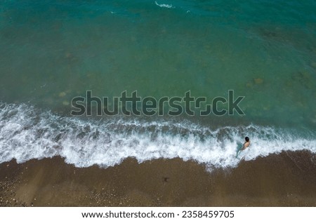 Woman with white dress walking on a sandy beach with braking waves on the shore. Aerial drone photograph. Paphos Cyprus