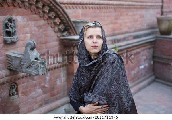 woman with white hair in a cashmere shawl stands in\
the garden near the house