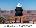 Woman with white hat on sandstone bench overlooking geological sandstone formations of Shafer Canyon within Canyonlands National Park near Moab, Utah, USA 