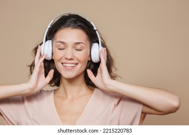 woman in white headphones on a beige background dances and sings to music. a beautiful European woman with curly hair listens to her favorite songs online or on the radio, podcast. audio content for - Shutterstock ID 2215220783