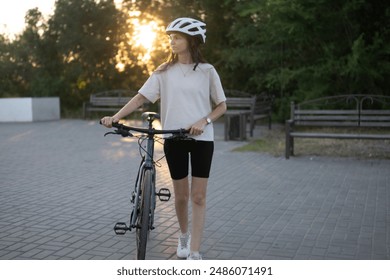 woman with a white helmet walks beside her bicycle on a paved path. She is wearing a white t-shirt, black shorts, and white sneakers - Powered by Shutterstock