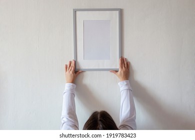 Woman In White Hoody Hanging Vertical Empty Frame On White Wall To Create Family Photo Gallery, To Capture A Moment, Mockup Template On White Background, Lifestyle